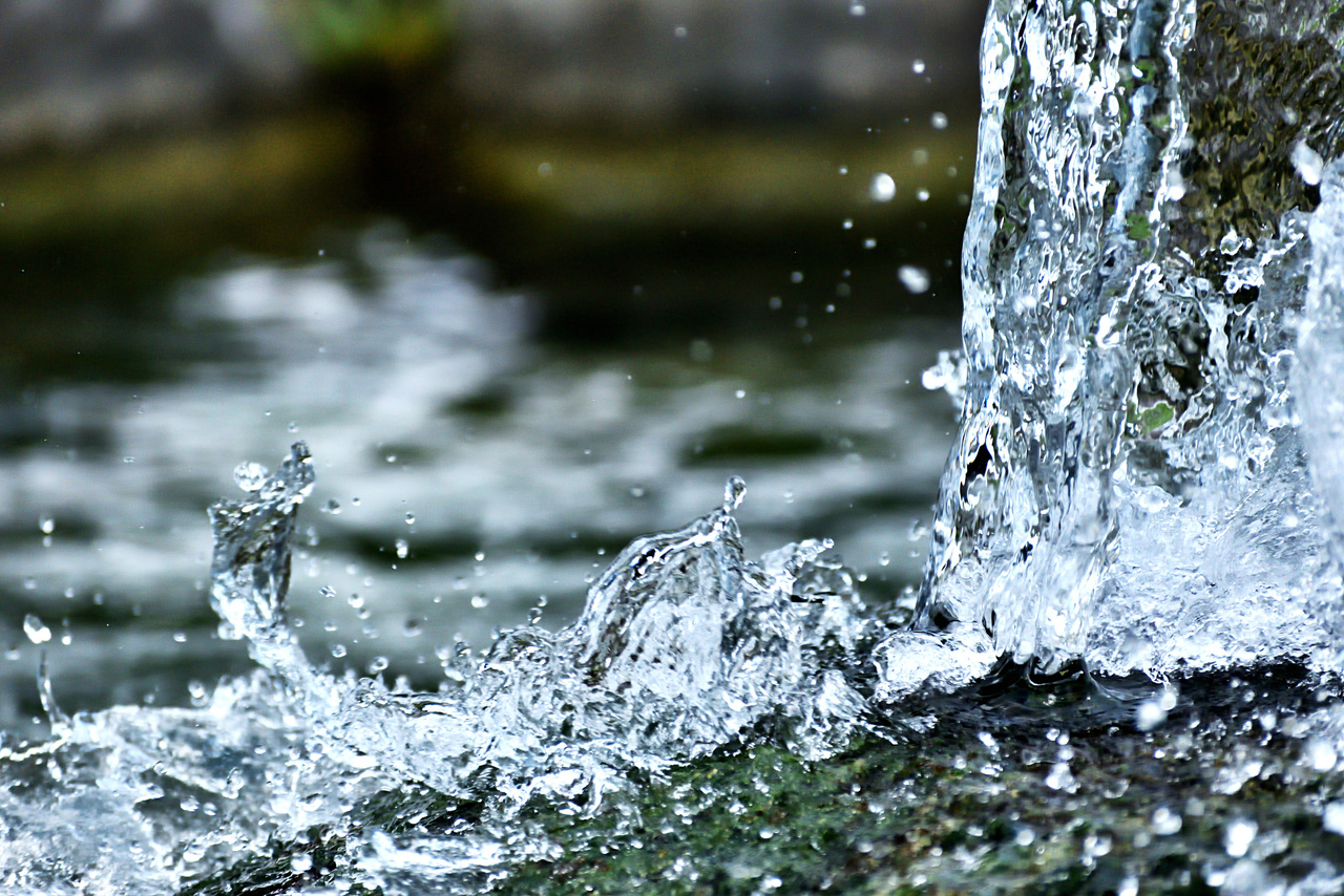 Ein klarer Wasserstrahl plätschert gegen einen dunkelgrünen Felsen und schafft eine dynamische und erfrischende Szene.