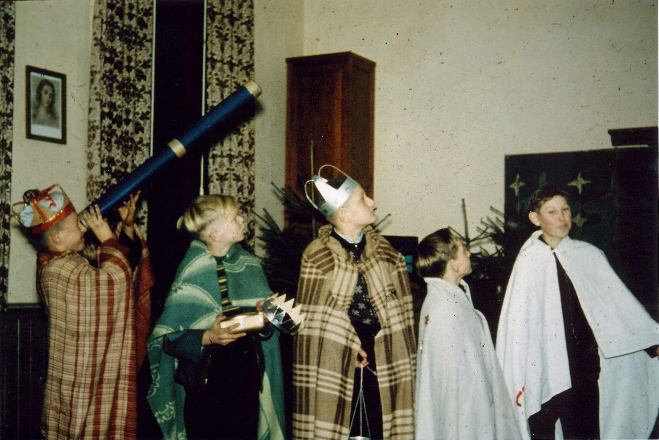 Kinder in Sternsinger-Kostümen, versammeln sich in einem Raum mit einem Holzschrank und einem gerahmten Bild.