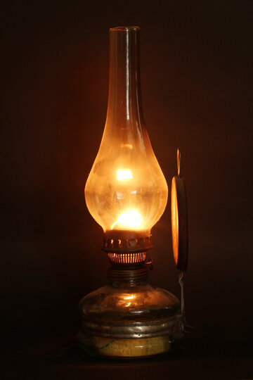 Eine alte Lampe mit Glasgefäß und Metallsockel strahlt einen warmen Schein aus und wirft ein sanftes Licht auf einen dunklen Hintergrund.