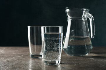 Ein Glaskrug und zwei mit Wasser gefüllte Gläser stehen auf einer dunkelgrauen Arbeitsplatte, wobei der Henkel des Kruges nach oben zeigt.