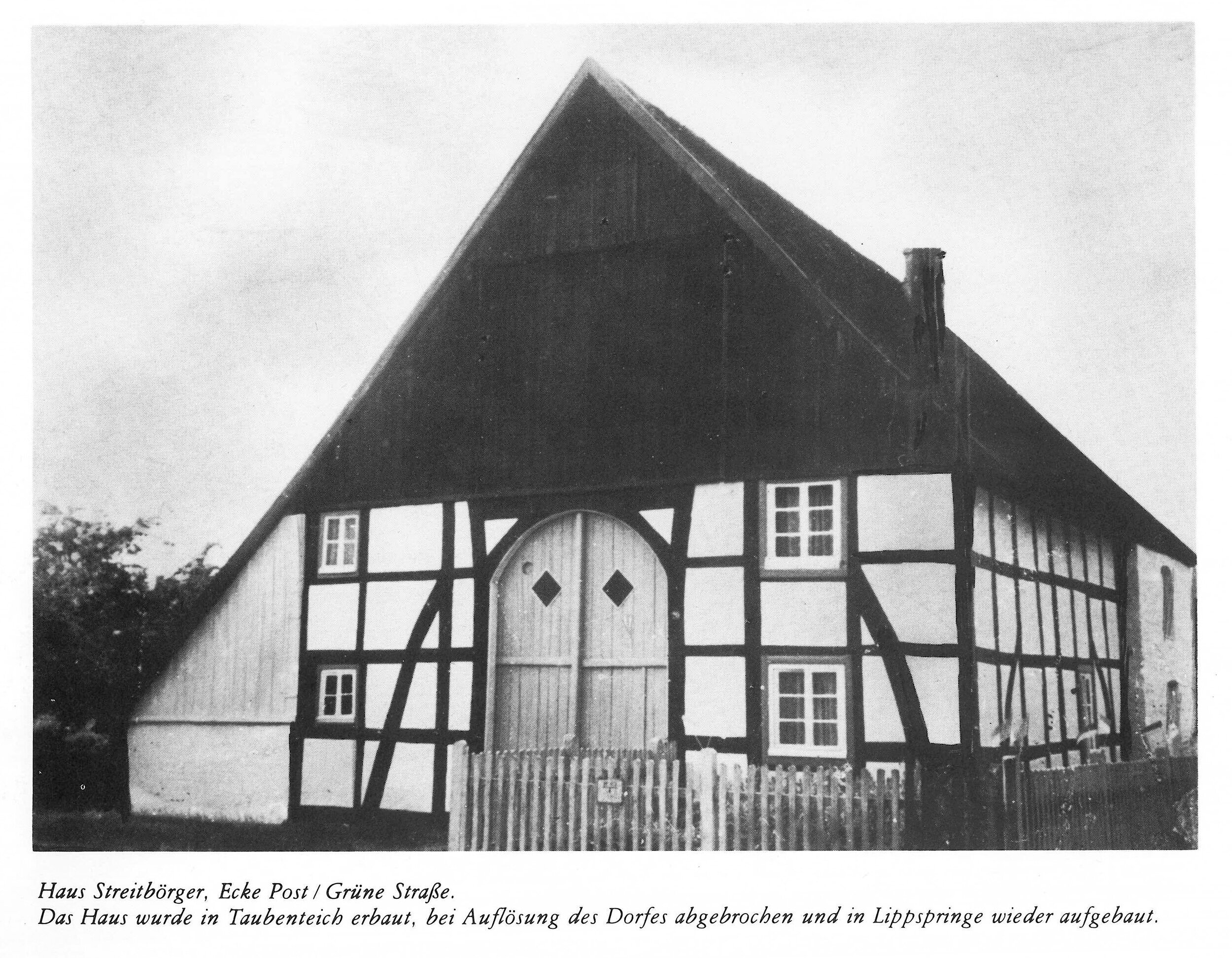 Eine Schwarz-Weiß-Fotografie eines Fachwerkhauses in Haus zeigt ein steiles Dach, weiße Wände und eine Holztür mit rautenförmigen Fenstern.