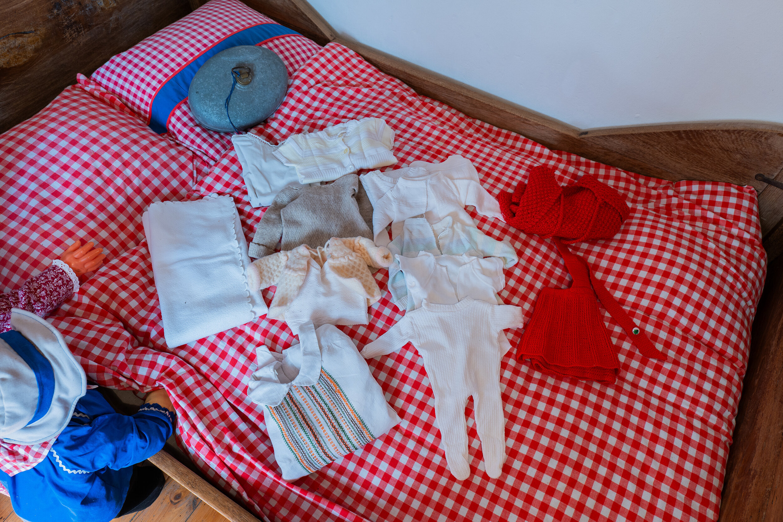 Zu sehen sind alte und traditionelle Baby- und Kinderkleidungsstücke aus der historischen Senne. Darunter gestrickte Jacken, Mützen und Pullover, sowie Strampler und Hemden aus Leinen.