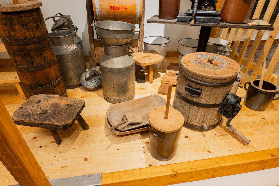 Auf dem Bild sind verschiedene traditionelle Werkzeuge zur Verarbeitung von Milchprodukten zu sehen. Darunter Butterfässer und Stampfer und unterschiedliche, metallene Milchkannen.
