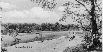 Ein Schwarz-Weiß-Foto von Haustenbeck, Deutschland, zeigt eine Person, die auf einem Hügel sitzt, einen Baum und ein Feld mit einer Kirche in der Ferne.